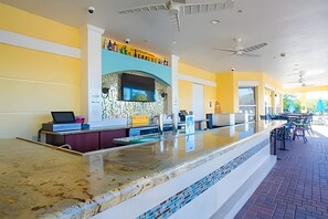 Un espace bar extérieur moderne, doté d’un long comptoir, de sièges et d’un ventilateur de plafond.