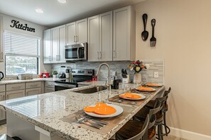 A modern kitchen with granite countertops, stainless steel appliances, and a central island with orange plates. - 3BR Terra Esmeralda Townhome, Free BBQ (Kissimmee)