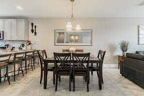 A modern kitchen with a dining area, featuring a central island, dark wooden chairs, and a chandelier. - 3BR Terra Esmeralda Townhome, Free BBQ (Kissimmee)