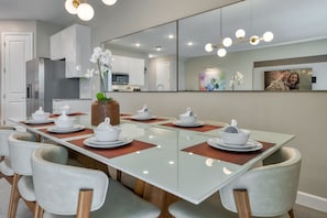 A modern dining area with a glass table, white chairs, and a large mirror above. - 4BR Villa w/ Pool Near Disney + Themed Rooms (Kissimmee)