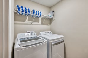 A laundry area with two front-loading washing machines and a drying rack with folded towels. - 4BR Villa w/ Pool Near Disney + Themed Rooms (Kissimmee)