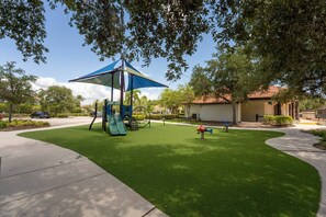 A playground with a slide and a swing set, surrounded by well-maintained grass and trees. - 4BR Bella Vida Lakeview Pool Townhome (Kissimmee)