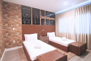 Habitació d'hotel amb dos llits, una paret de maó i una finestra gran amb cortines.