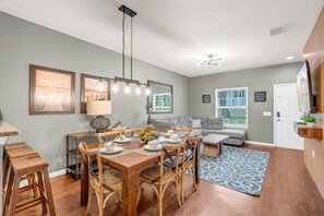 A dining area with a wooden table and chairs, a sofa, and a patterned rug. - 3BR Lucaya Village Home Near Disney (Kissimmee)