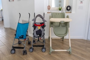 A room with a wooden floor, a blue stroller, a gray stroller, and a green baby seat. - Single-story 4BR Home w/ Pool & Game Room (Kissimmee)