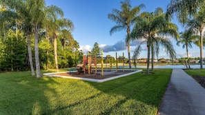 A playground with a climbing structure and swings, surrounded by palm trees and a clear sky. - Single-story 4BR Home w/ Pool & Game Room (Kissimmee)