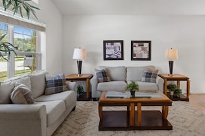 A living room with a sofa, two side tables, a coffee table, and two wall-mounted lamps. There are two framed abstract artworks on the wall. - 4BR Home w/ Private Pool & Spa Near Disney (Kissimmee)