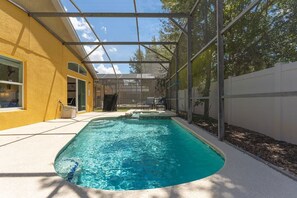 A swimming pool with a glass enclosure, surrounded by a yellow building and a white fence. - 4BR Home w/ Private Pool & Spa Near Disney (Kissimmee)