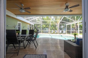 A covered patio with a pool, ceiling fans, a dining area with chairs and a table, and a wicker sofa. - Anna Maria Beach House Steps to Sand (Holmes Beach)