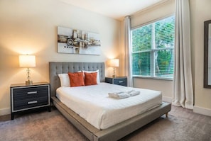 A bedroom with a bed, two bedside tables, a window with blinds, and a wall-mounted artwork. - 4BR Home w/ Private Pool Hidden Forest (Clermont)
