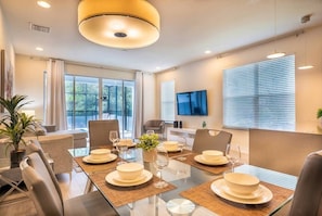 A modern dining area with a glass table, chairs, and a central light fixture. - 4BR Home w/ Private Pool Hidden Forest (Clermont)