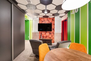 A conference room with a modern design, featuring a hexagonal ceiling, a flat-screen TV, and a green accent wall. - 3BR Themed Home Near Disney (Kissimmee)