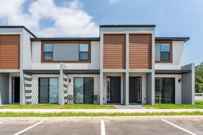 A modern multi-story residential building with large windows, a flat roof, and a parking area in front. - 3BR Themed Home Near Disney (Kissimmee)