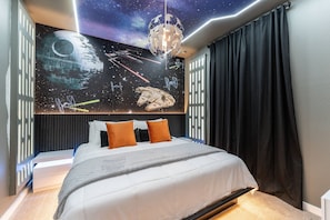 A bedroom with a Star Wars-themed wall mural, a bed with white bedding and orange pillows, and a modern ceiling light fixture. - 3BR Themed Home Near Disney (Kissimmee)