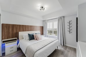 A bedroom with a bed, bedside table, and a window with curtains. - Resort Suite on International Drive (Orlando)