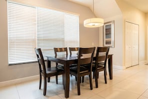 Un comedor con una mesa y sillas, una ventana con persianas, una lámpara colgante y una puerta.