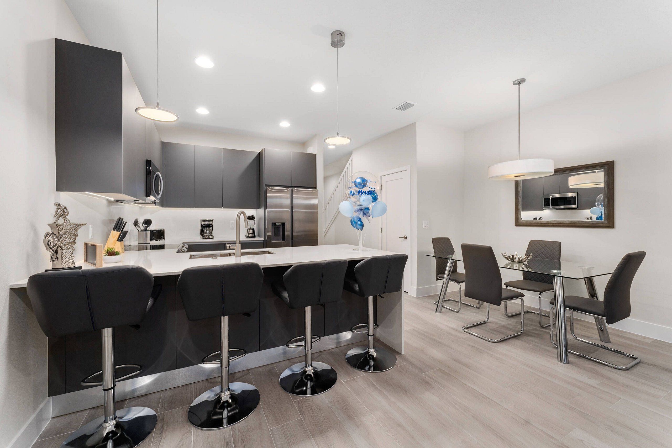 A modern kitchen with a central island, bar stools, a dining table with chairs, and a microwave above the island.