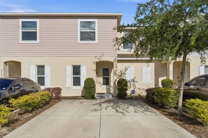 A two-story residential building with a beige exterior, white shutters, and a front entrance. - Fiesta Key 3BR Townhome Near Disney (Kissimmee)
