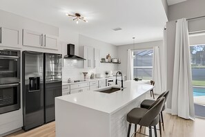 A modern kitchen with a central island, stainless steel appliances, and a view to the outdoors. - Windsor Hills 5BR Luxury Pool & Game Room (Kissimmee)