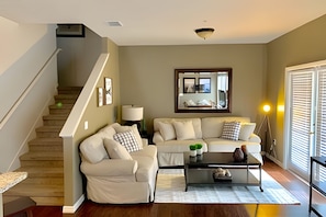 A living room with a staircase, a sofa set, a coffee table, a lamp, and a large mirror. - 4BR Townhouse at Lucaya With Resort Pool (Kissimmee)