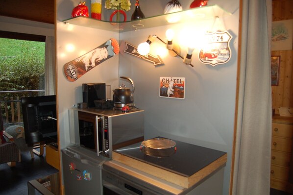 A compact kitchen with a microwave, kettle, and a small refrigerator. There are decorative items and a sign that reads 'CHÂTEL' on the wall.