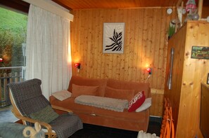 A wooden-paneled room with a sofa, a chair, and a wall-mounted light fixture. - Central accommodation near the pool (Châtel)