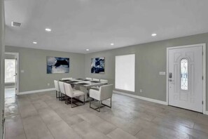A spacious room with a large dining table and chairs, a white door with a glass panel, and two abstract paintings on the walls. - 5BR Lakeview Home w/ Pool 3min to Universal (Orlando)
