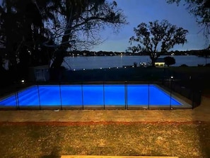 A rectangular swimming pool with a blue tint, surrounded by a metal fence and a grassy area. - 5BR Lakeview Home w/ Pool 3min to Universal (Orlando)