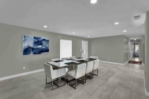 A spacious dining area with a long table and white chairs, a large abstract painting on the wall, and a door leading to another room. - 5BR Lakeview Home w/ Pool 3min to Universal (Orlando)