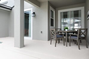 A patio area with a table and chairs, a potted plant, and a sliding glass door leading to an interior space. - Chic 4BR Home Storey Lake - Near Disney (Kissimmee)