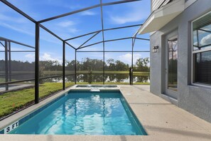 A swimming pool with a clear blue water, surrounded by a covered area with a metal frame and glass panels. - Reunion 5BR Home w/ Pool 15min to Disney (Kissimmee)
