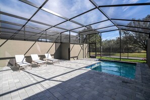 Un espace piscine extérieur doté d’une structure en verre, de chaises longues et offrant une vue sur le paysage environnant.