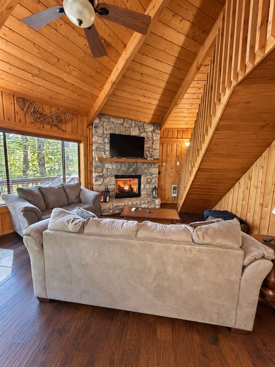 A cozy living room with a stone fireplace, a large beige sofa, and a ceiling fan.