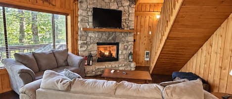 A cozy living room with a stone fireplace, a large beige sofa, and a ceiling fan.