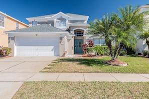 A two-story house with a garage, a front door, and a well-maintained lawn with palm trees. - 5BR Lake Berkley Home, Lake-view Pool (Kissimmee)