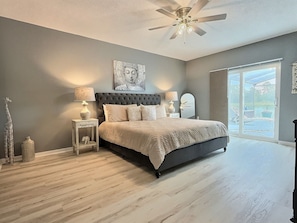 A bedroom with a large bed, a ceiling fan, a nightstand with a lamp, and a view of a balcony. - 5BR Lake Berkley Home, Lake-view Pool (Kissimmee)