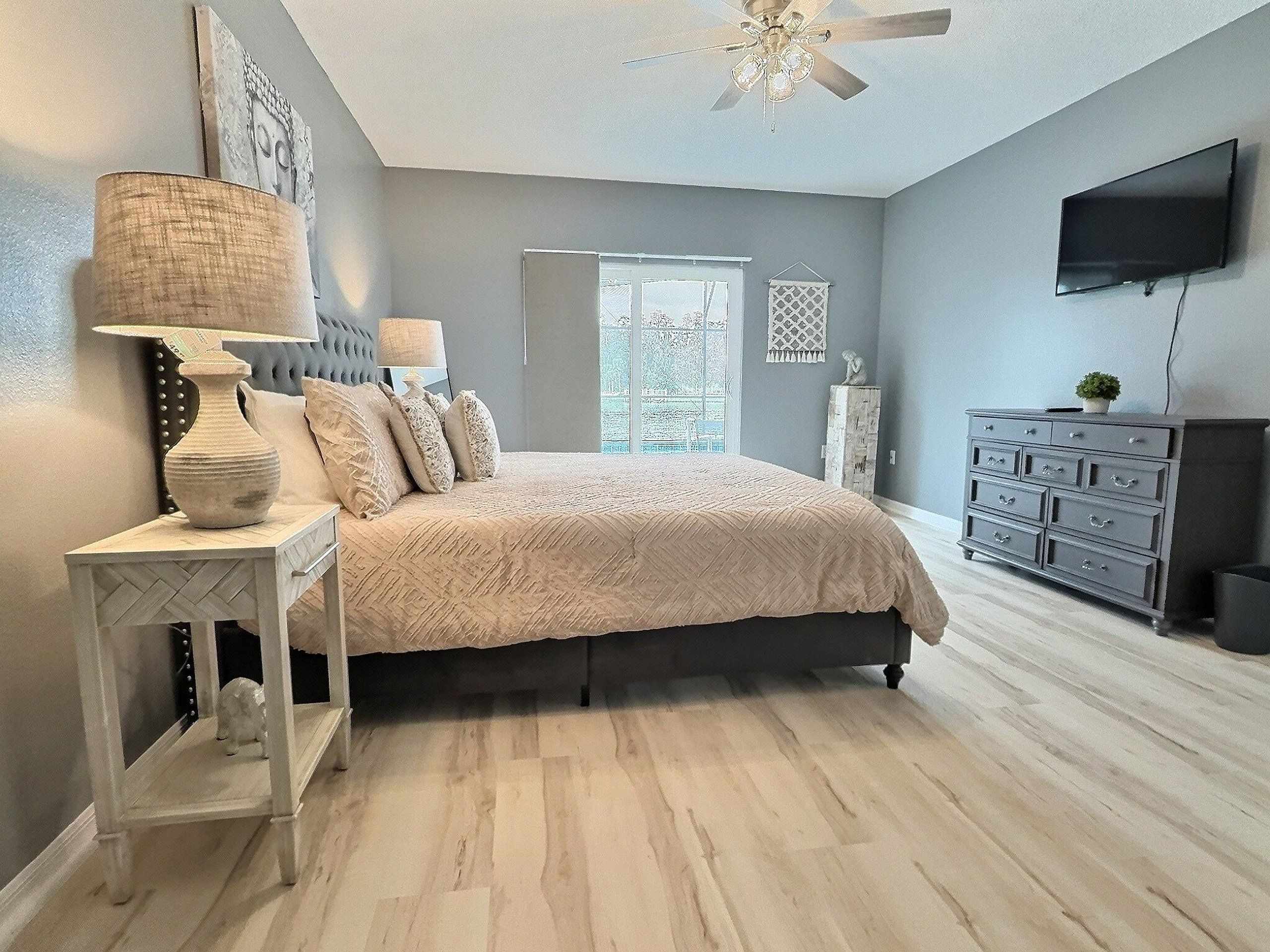 A bedroom with a bed, bedside tables, a dresser, a ceiling fan, and a TV.