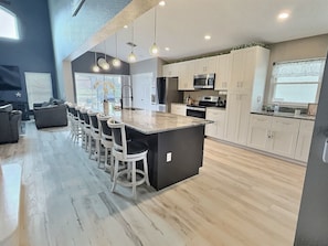 A modern kitchen with a central island, bar stools, and a dining area with a view. - 5BR Lake Berkley Home, Lake-view Pool (Kissimmee)