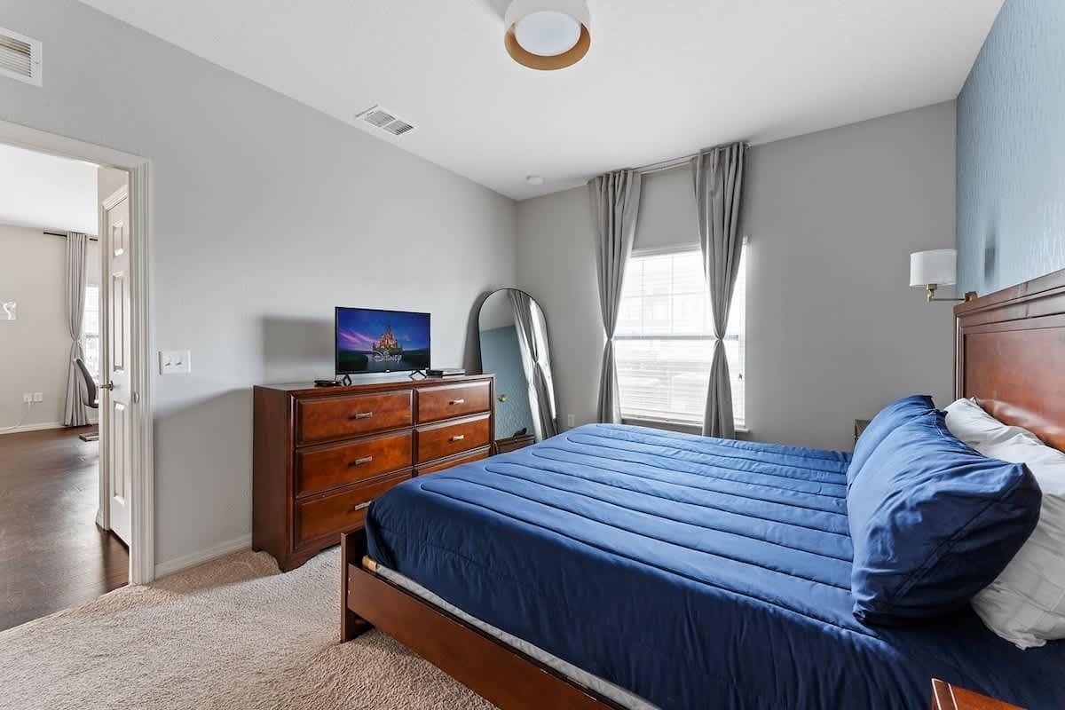 A bedroom with a large bed, a dresser, a television, and a mirror.