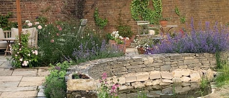 Un jardín con macetas de piedra, un muro de ladrillo y un pérgola.