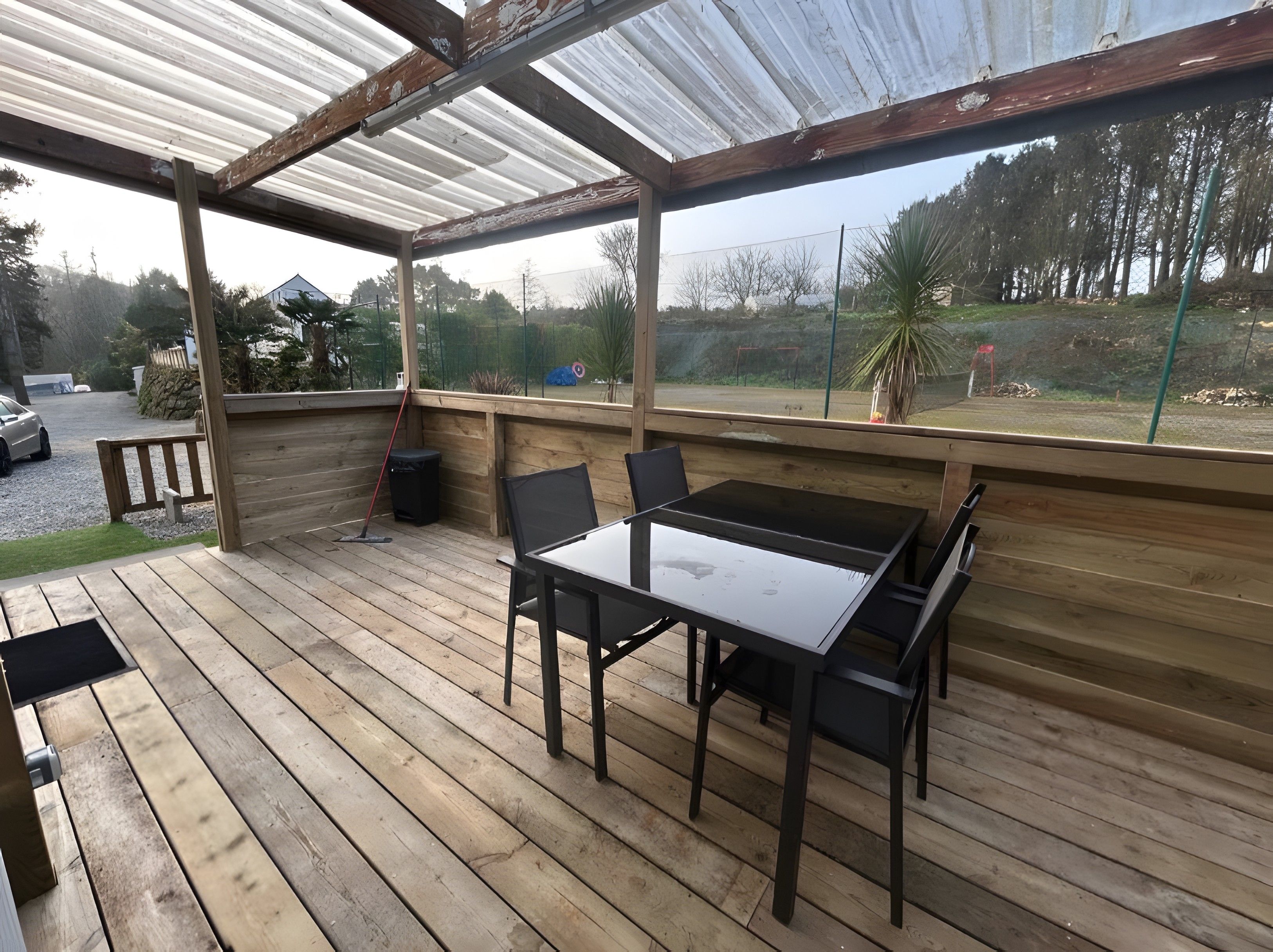 Un área de estar al aire libre con techo, una mesa, sillas, una terraza de madera y vistas del paisaje circundante.
