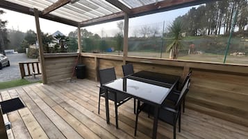 Un área de estar al aire libre con techo, una mesa, sillas, una terraza de madera y vistas del paisaje circundante.