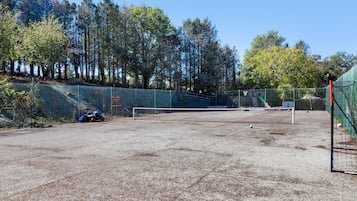 Una cancha de tenis exterior con red, rodeada por una valla y árboles.