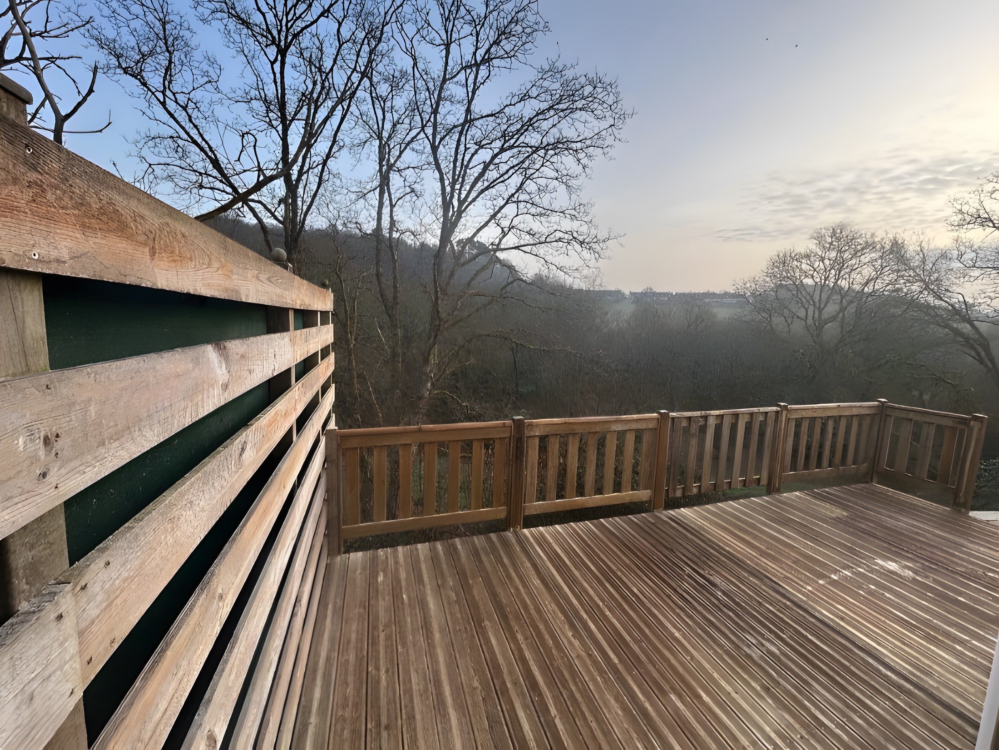 Eine Holzdielen-Terrasse mit Geländer, die auf einen bewaldeten Bereich blickt.