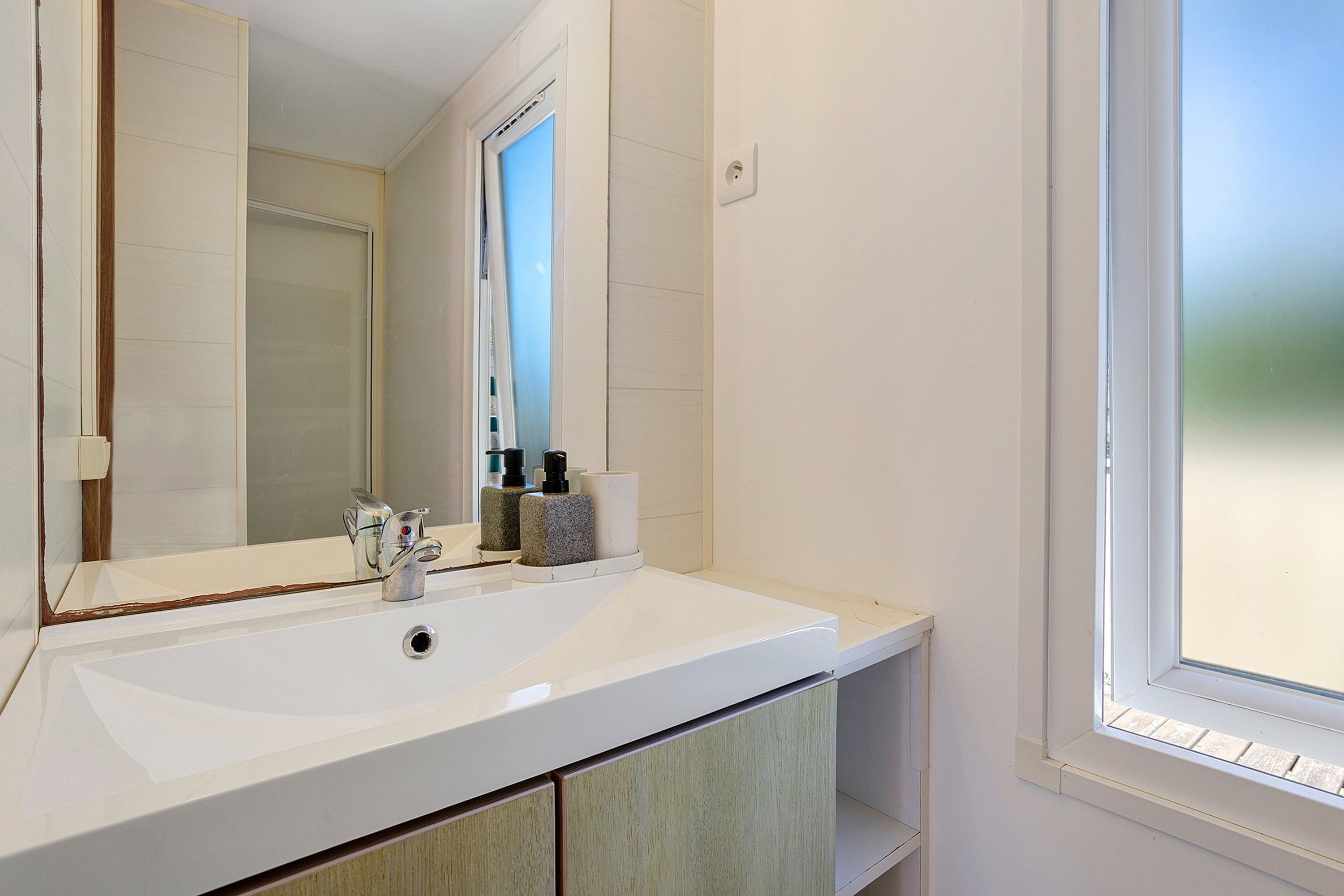 Un baño con un lavabo blanco, un espejo y una ventana.