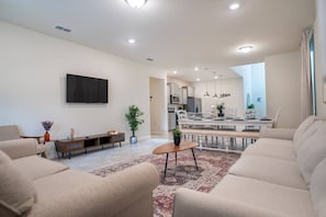 A modern living room with a flat-screen TV, sofas, a coffee table, and a dining area with a table and chairs. - 6BR Disney Home w/ Pool at Windsor Cay (Clermont)