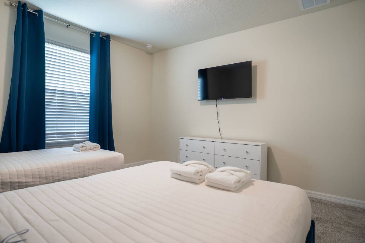 Ein Hotelzimmer mit zwei Betten, einem flachbildfernseher an der Wand und einer weißen Kommode.