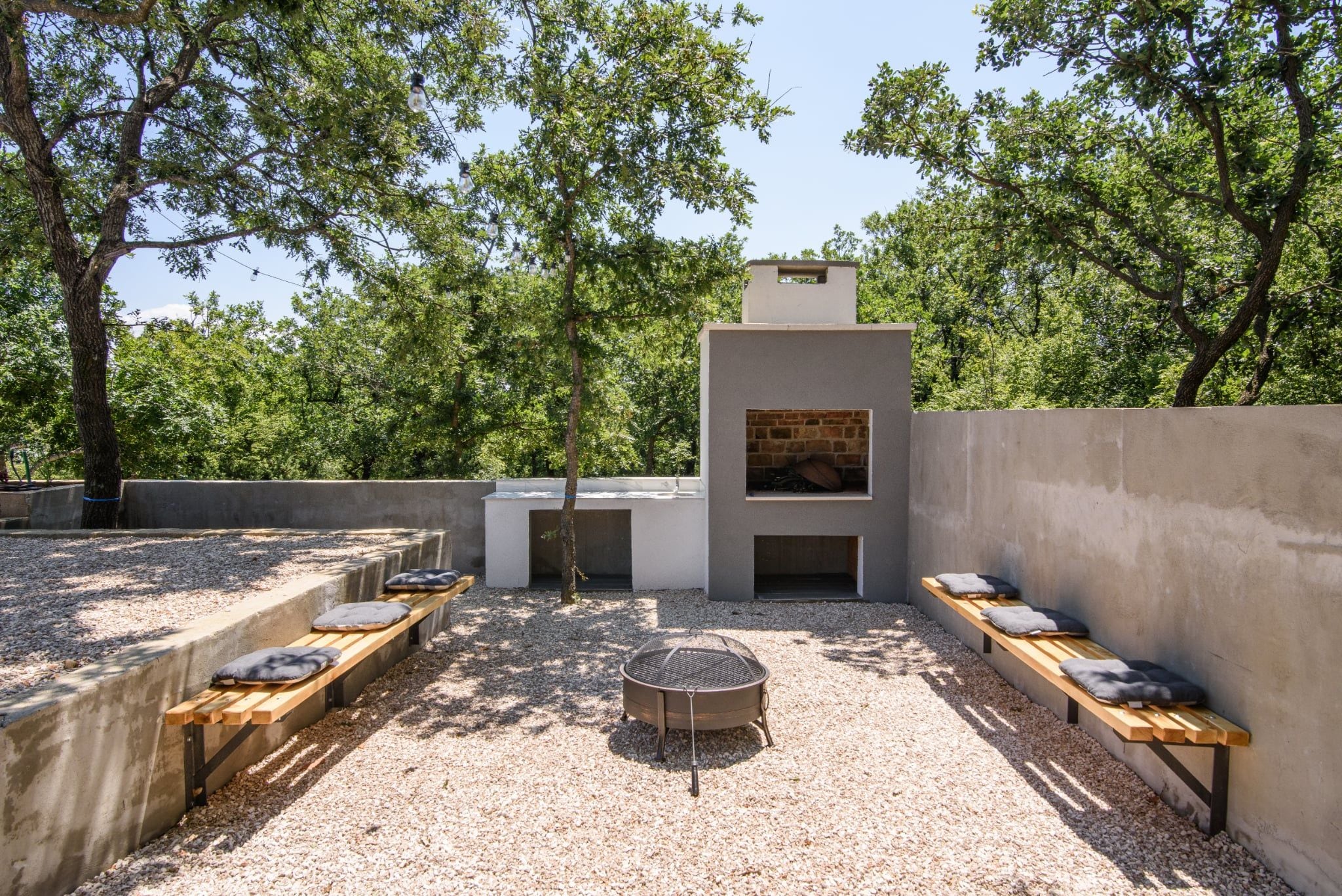 An outdoor patio with a built-in grill, seating, and a view of trees.