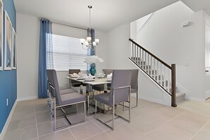 A modern dining area with a table and chairs, a staircase, and a window with blinds. - HMU - 1799 - Luxurious 7br/6ba Solara Resort (Kissimmee)