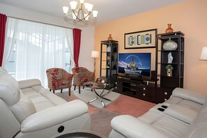 A living room with a sofa set, a TV, and a decorative shelf. - 6BR Townhome w/ Pool 10 Min to Disney (Kissimmee)